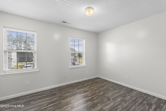 empty room with a textured ceiling, baseboards, wood finished floors, and visible vents