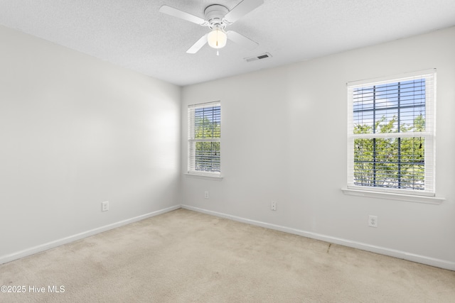 spare room featuring ceiling fan, a textured ceiling, visible vents, baseboards, and light carpet