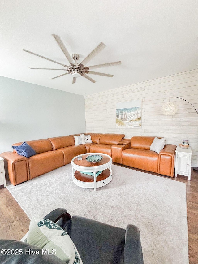 living area featuring ceiling fan, wood finished floors, and wooden walls