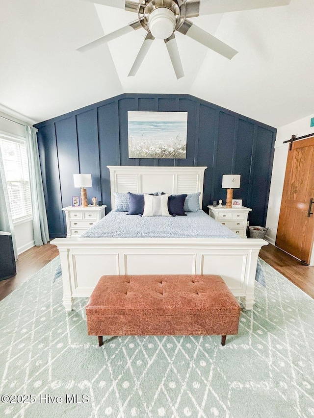 bedroom with wood finished floors, a barn door, a decorative wall, and lofted ceiling