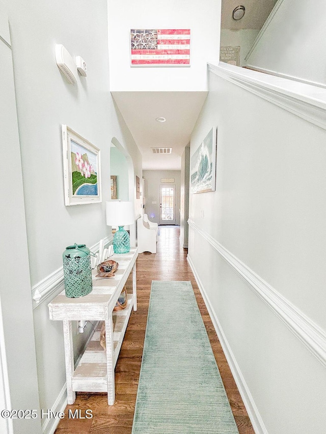 hallway with arched walkways, baseboards, visible vents, and wood finished floors