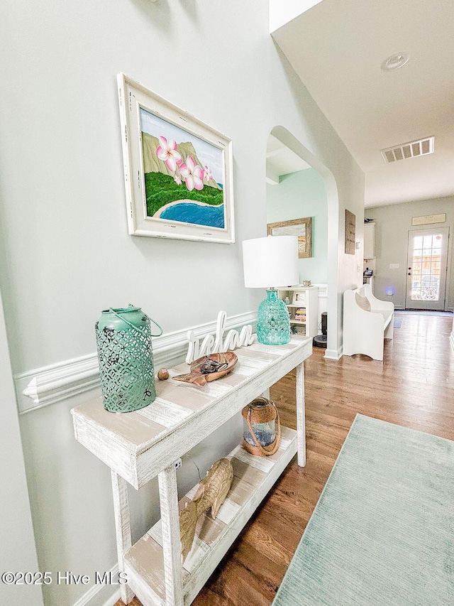 hall featuring visible vents, arched walkways, baseboards, and wood finished floors