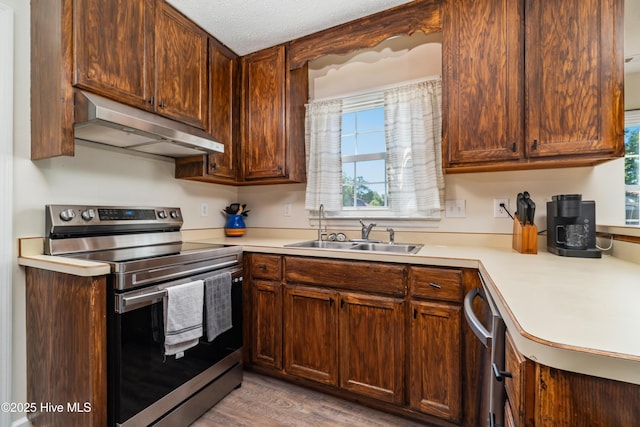 kitchen with a sink, light countertops, stainless steel appliances, and under cabinet range hood