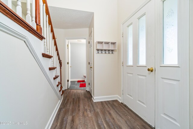 foyer entrance with stairs, a textured ceiling, baseboards, and dark wood finished floors