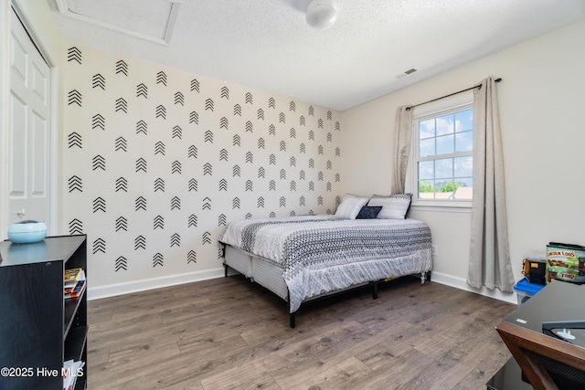 bedroom with baseboards, attic access, wood finished floors, and visible vents