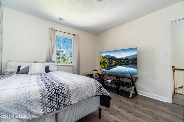bedroom featuring baseboards, a textured ceiling, wood finished floors, and visible vents