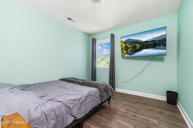 bedroom with baseboards, dark wood-style flooring, a textured ceiling, and visible vents