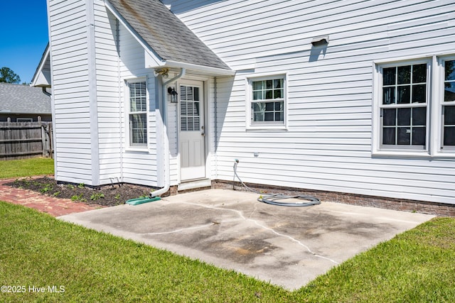 property entrance featuring fence, a yard, a patio area, and roof with shingles