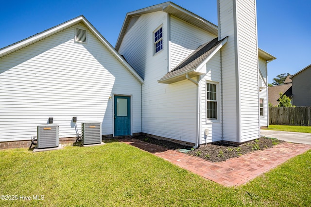 rear view of house featuring a lawn, central air condition unit, a chimney, and fence