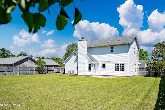 rear view of house with a lawn, a fenced backyard, a chimney, and a patio