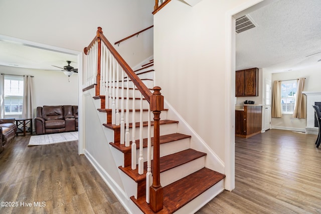 stairway with plenty of natural light, ceiling fan, wood finished floors, and visible vents