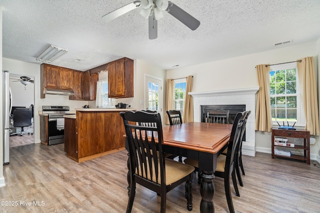 dining area featuring a textured ceiling, ceiling fan, visible vents, and light wood finished floors
