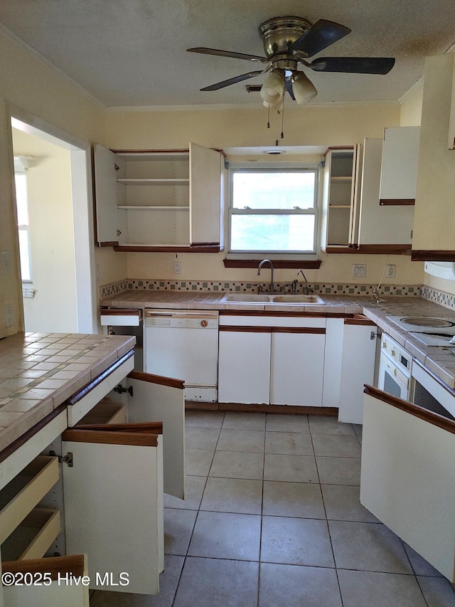 kitchen featuring ceiling fan, tile countertops, white dishwasher, a sink, and white cabinets