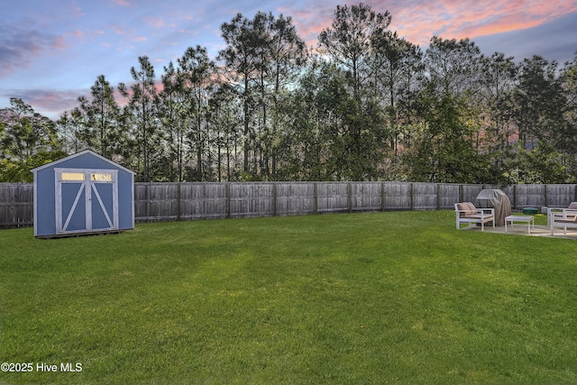 yard at dusk with a fenced backyard, a patio area, a storage shed, and an outbuilding