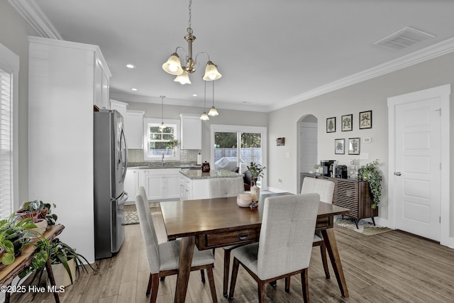 dining space with crown molding, light wood-type flooring, visible vents, arched walkways, and a chandelier