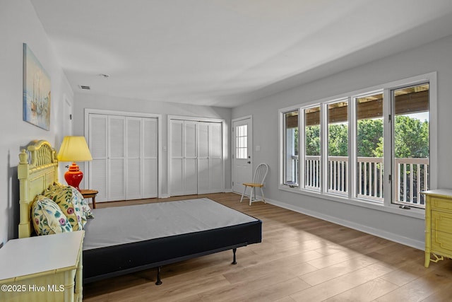 bedroom featuring two closets, baseboards, and light wood finished floors