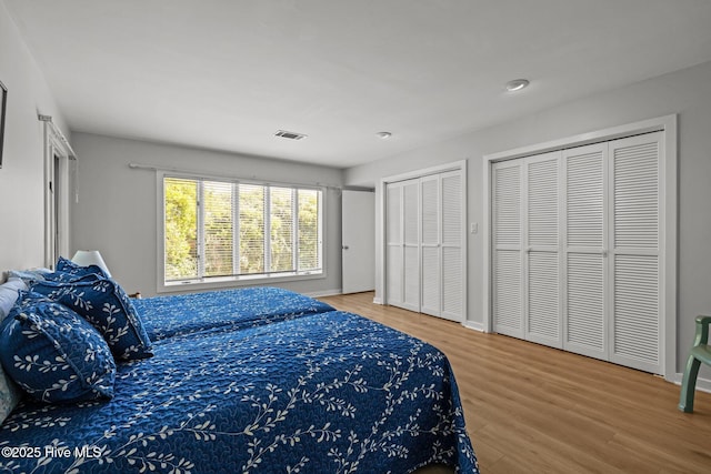 bedroom featuring baseboards, two closets, wood finished floors, and visible vents