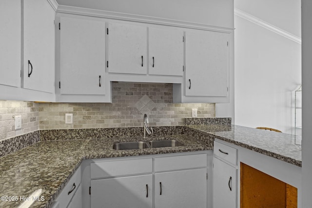 kitchen featuring a sink, white cabinetry, dark stone countertops, and backsplash
