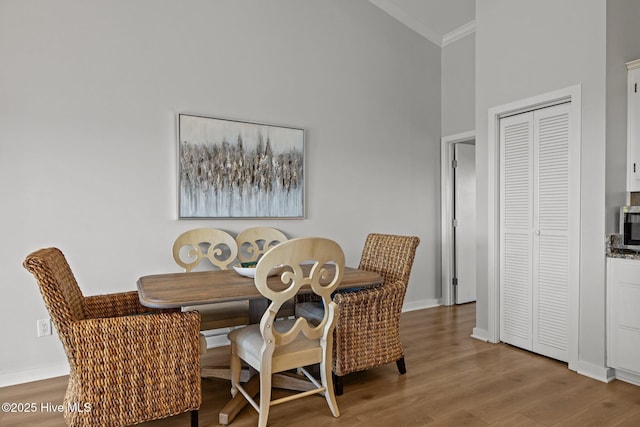 dining room with baseboards, ornamental molding, wood finished floors, and a towering ceiling