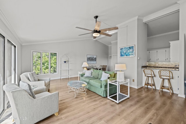 living area featuring a ceiling fan, vaulted ceiling, wood finished floors, baseboards, and ornamental molding