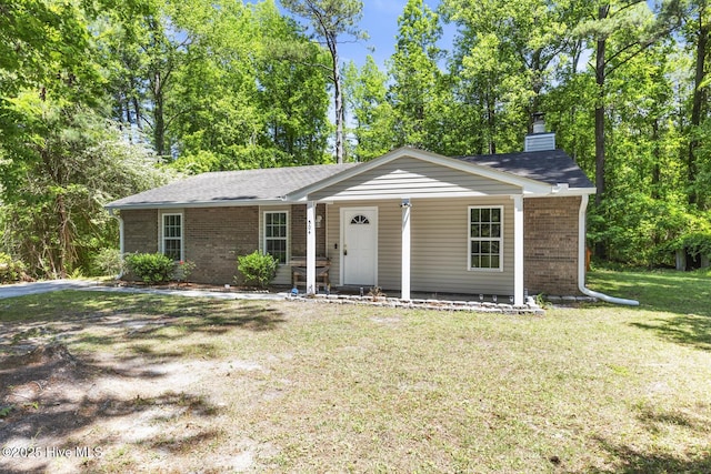 ranch-style house featuring covered porch, a chimney, a front yard, and brick siding