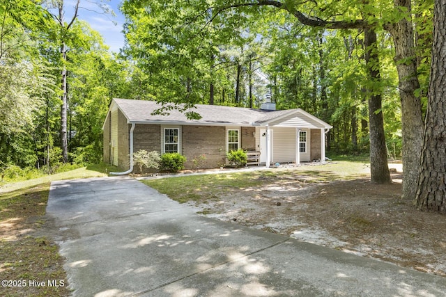 single story home featuring covered porch, brick siding, driveway, and a chimney