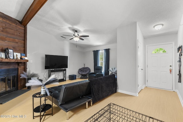 living room featuring a ceiling fan, a textured ceiling, a glass covered fireplace, and baseboards
