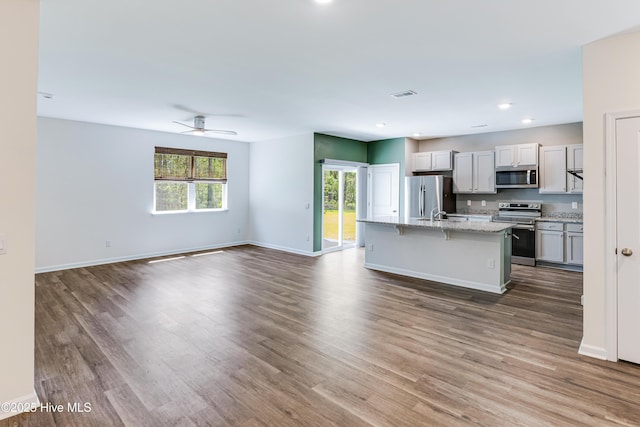 kitchen with a kitchen island with sink, open floor plan, appliances with stainless steel finishes, and wood finished floors