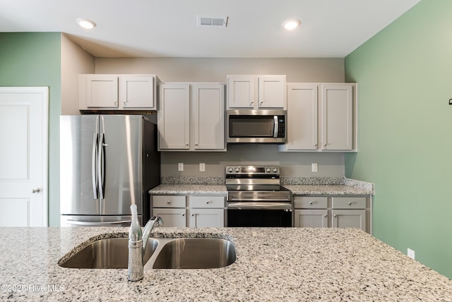 kitchen with appliances with stainless steel finishes, light stone counters, a sink, recessed lighting, and visible vents
