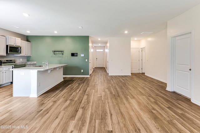 kitchen featuring a kitchen island with sink, recessed lighting, a sink, light wood-style flooring, and appliances with stainless steel finishes