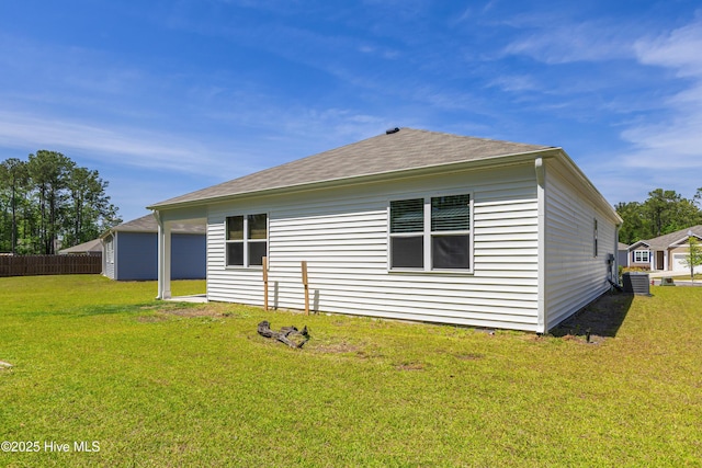 rear view of house featuring a lawn, central AC unit, roof with shingles, and fence