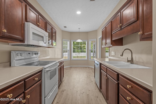 kitchen featuring a sink, light wood finished floors, white appliances, and light countertops