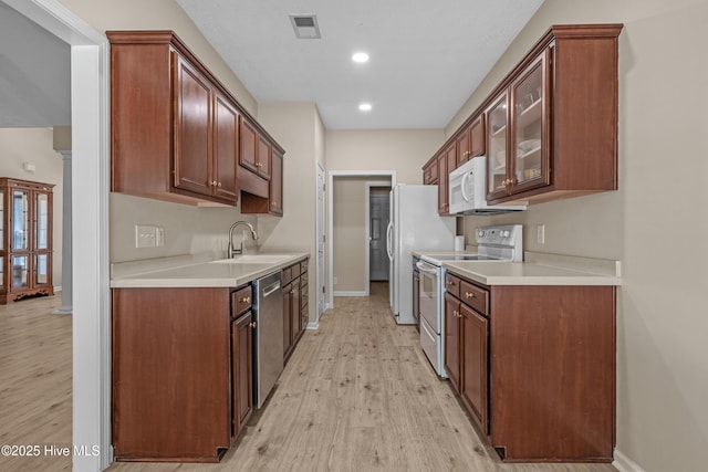 kitchen with a sink, light wood-style floors, white appliances, baseboards, and visible vents