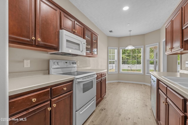 kitchen with hanging light fixtures, light countertops, baseboards, white appliances, and light wood-style flooring