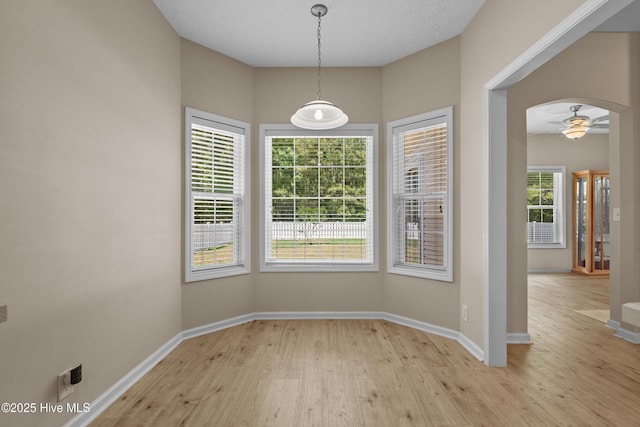 unfurnished dining area featuring baseboards, ceiling fan, and light wood finished floors