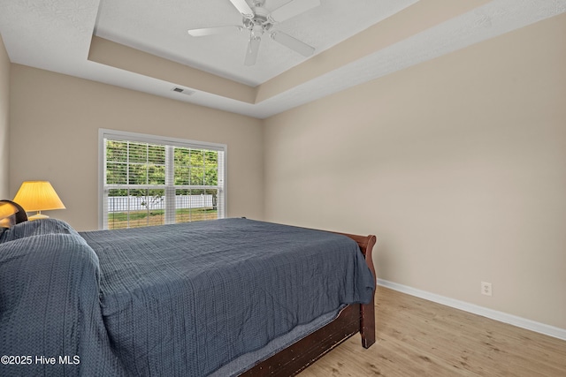 bedroom featuring a ceiling fan, baseboards, wood finished floors, a tray ceiling, and visible vents