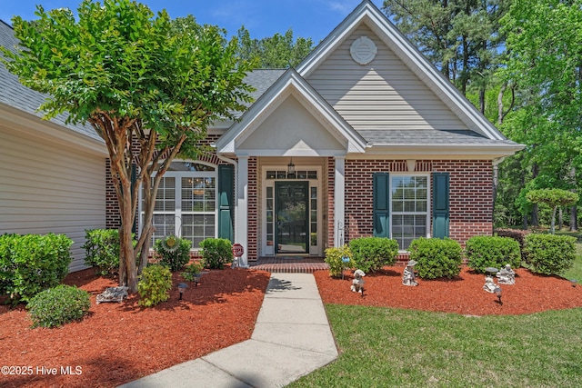 view of front of house with brick siding, a shingled roof, covered porch, and a front yard