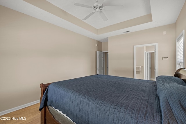bedroom with light wood-style flooring, a ceiling fan, baseboards, a tray ceiling, and visible vents