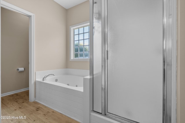full bath featuring baseboards, a tub with jets, wood finished floors, and a stall shower