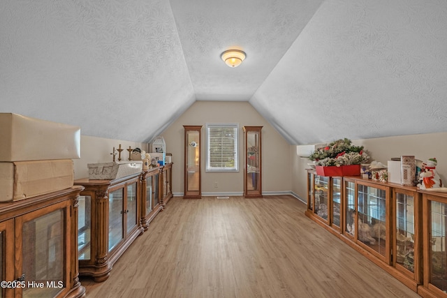 additional living space with baseboards, a textured ceiling, lofted ceiling, and wood finished floors