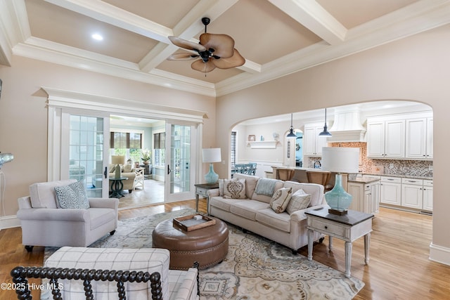 living room with arched walkways, ceiling fan, light wood-style flooring, coffered ceiling, and beam ceiling