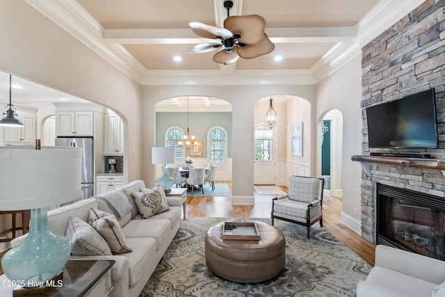 living area featuring arched walkways, ornamental molding, a chandelier, ceiling fan, and light wood-style flooring