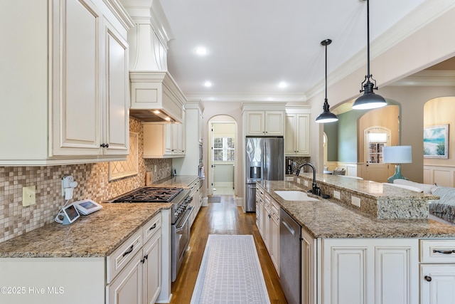 kitchen featuring appliances with stainless steel finishes, a sink, arched walkways, premium range hood, and light wood finished floors