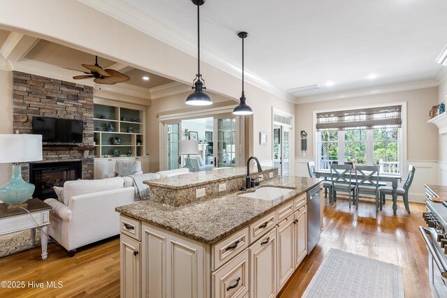 kitchen with a sink, a stone fireplace, cream cabinetry, appliances with stainless steel finishes, and ceiling fan