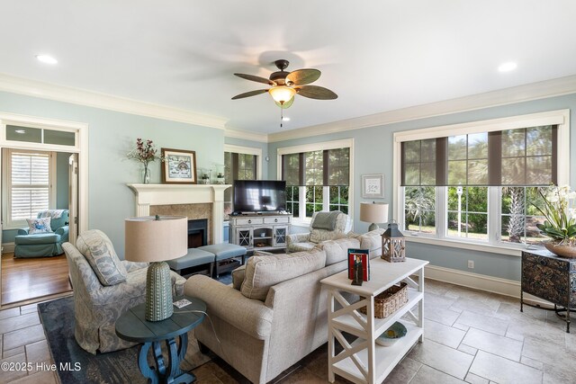 living room with a fireplace, crown molding, baseboards, ceiling fan, and stone tile flooring