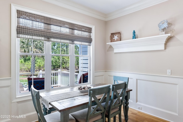 dining area featuring a decorative wall, ornamental molding, wainscoting, and wood finished floors