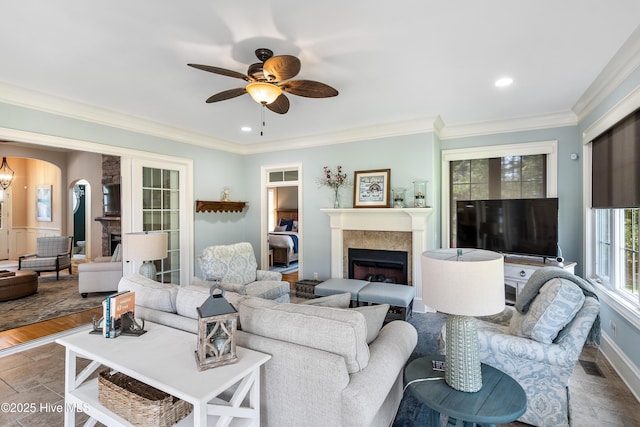 living area featuring a fireplace, ceiling fan, arched walkways, ornamental molding, and stone finish floors