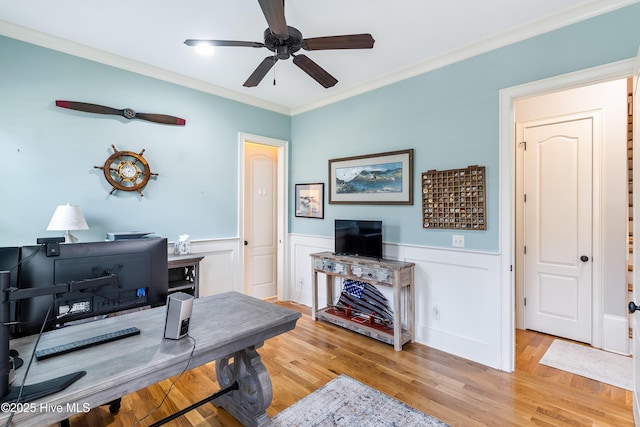 home office with ceiling fan, a wainscoted wall, light wood-style floors, and crown molding