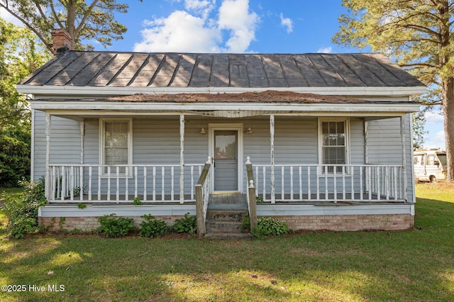 view of front facade with a porch, a front yard, a chimney, and a standing seam roof