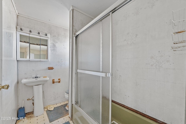 bathroom featuring toilet, tile walls, a sink, and bath / shower combo with glass door